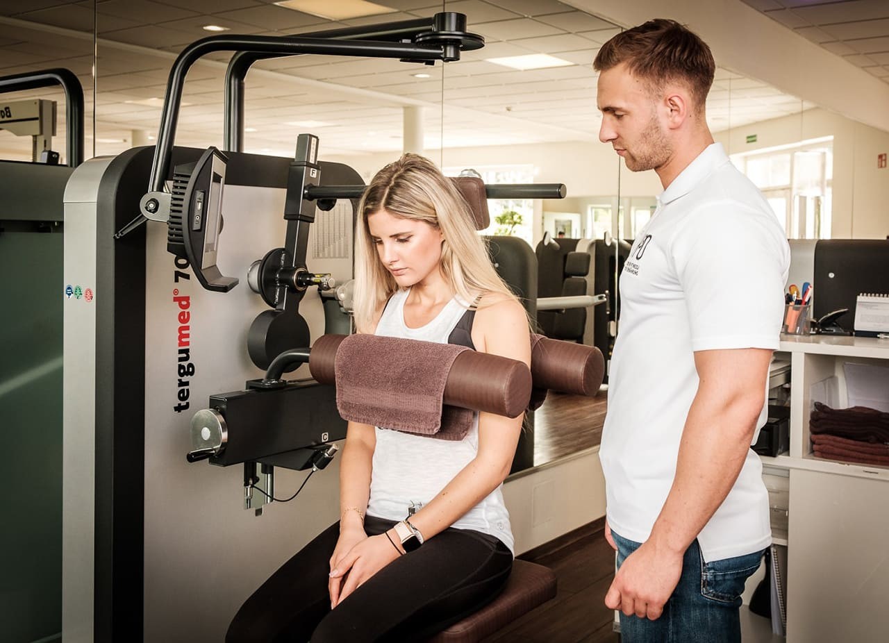Trainer erklärt einer Frau eine Übung am Trainingsgerät
